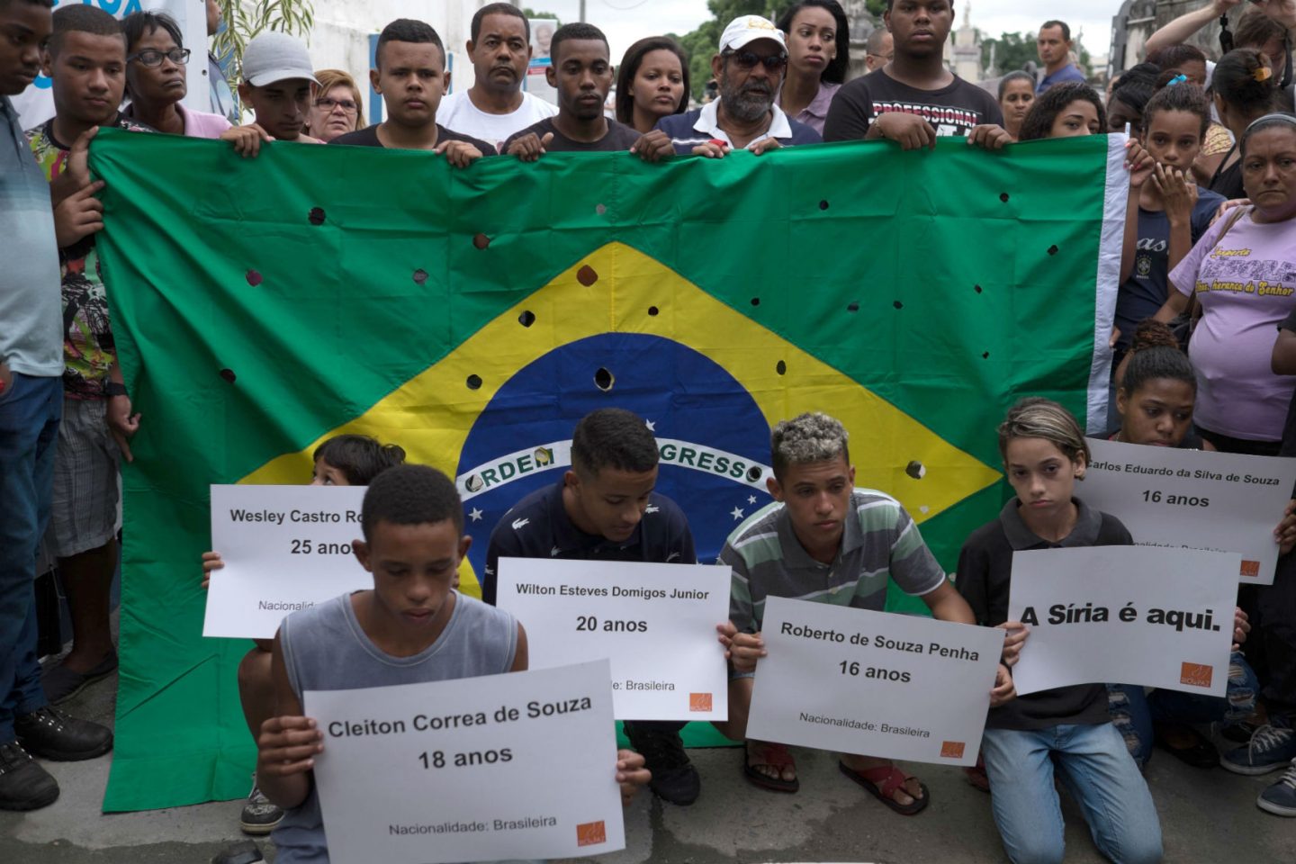 Parentes e amigos dos jovens assassinados por policiais militares posam com cartazes e uma bandeira com 50 tiros