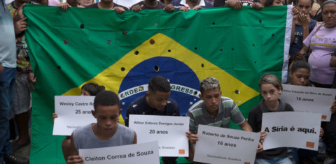 Parentes e amigos dos jovens assassinados por policiais militares posam com cartazes e uma bandeira com 50 tiros