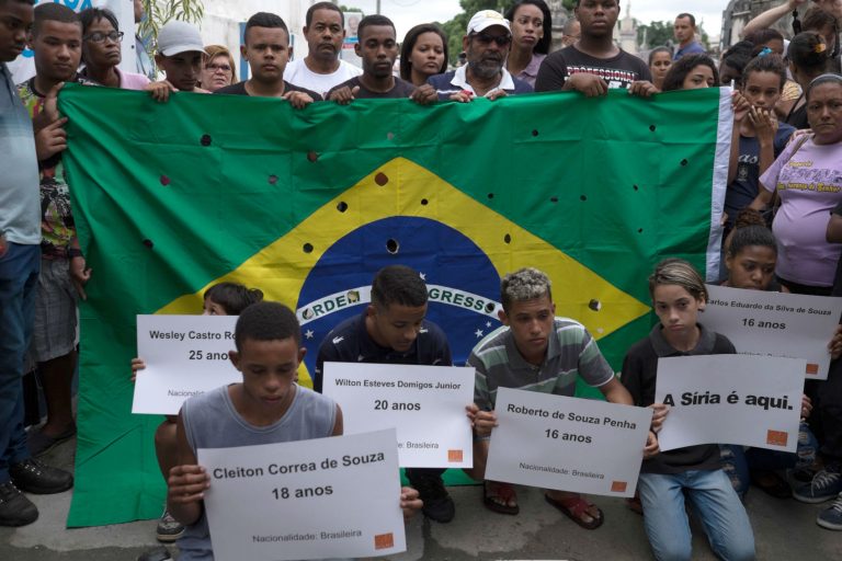 Parentes e amigos dos jovens assassinados por policiais militares posam com cartazes e uma bandeira com 50 tiros