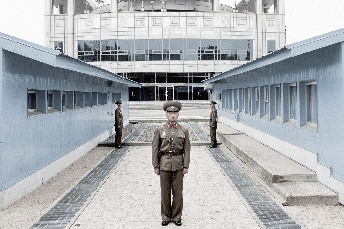 Panmunjon, fronteira entre Coréia do norte e do sul. A linha de concreto abaixo dos dois militares marca a fronteira. O prédio ao fundo já é da Coreia do sul