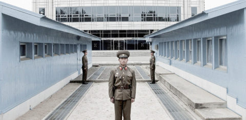 Panmunjon, fronteira entre Coréia do norte e do sul. A linha de concreto abaixo dos dois militares marca a fronteira. O prédio ao fundo já é da Coreia do sul
