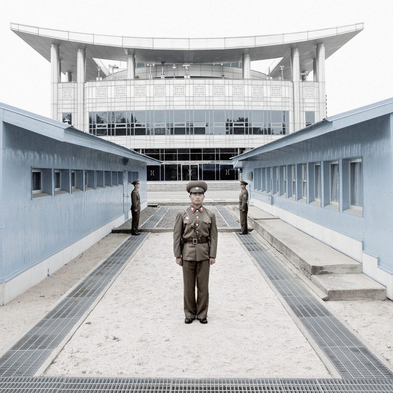 Panmunjon, fronteira entre Coréia do norte e do sul. A linha de concreto abaixo dos dois militares marca a fronteira. O prédio ao fundo já é da Coreia do sul