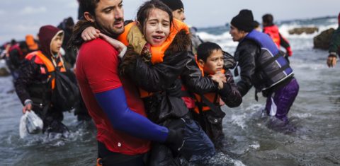 Voluntário segura uma menina que chegado com sua família e outros refugiados afegãos à ilha de Lesvos, na Grécia