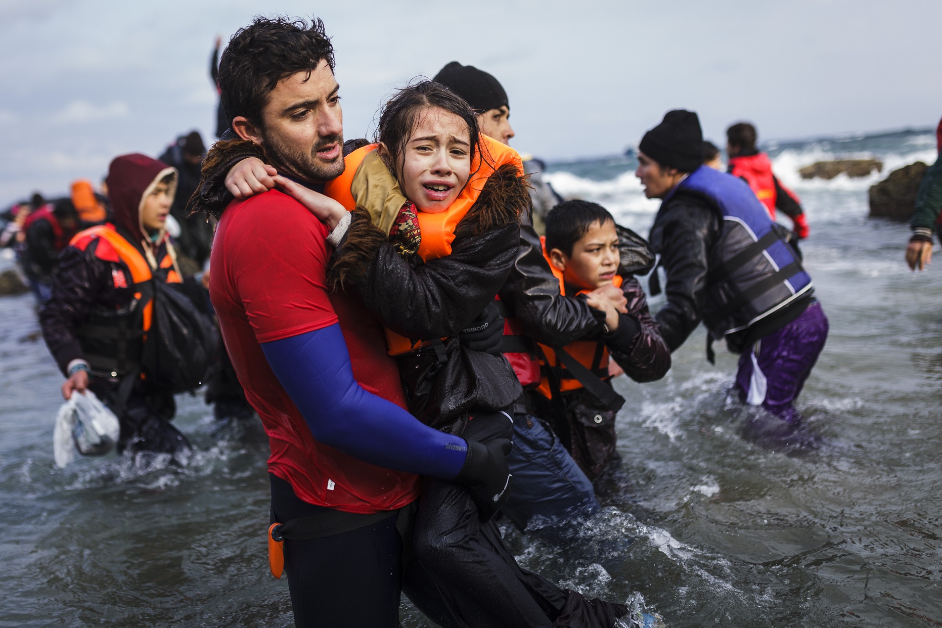Voluntário segura uma menina que chegado com sua família e outros refugiados afegãos à ilha de Lesvos, na Grécia