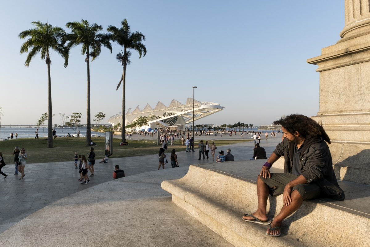 Um homem sentado num monumento observa as pessoas passeando em torno do Museu do Amanhã. Foto de Peter Bauza/DPA