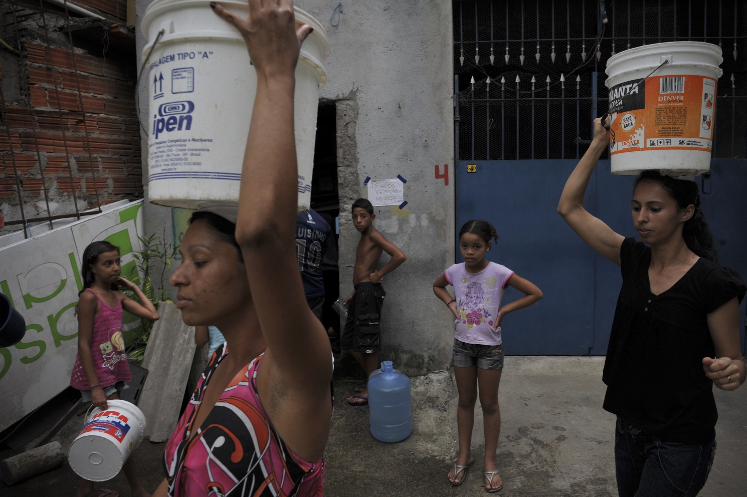 Mulheres carregam baldes na cabeça na favela de Paraisópolis, em São Paulo: acesso a água precisa ser universalizado. Foto Maurício Lima/AFP