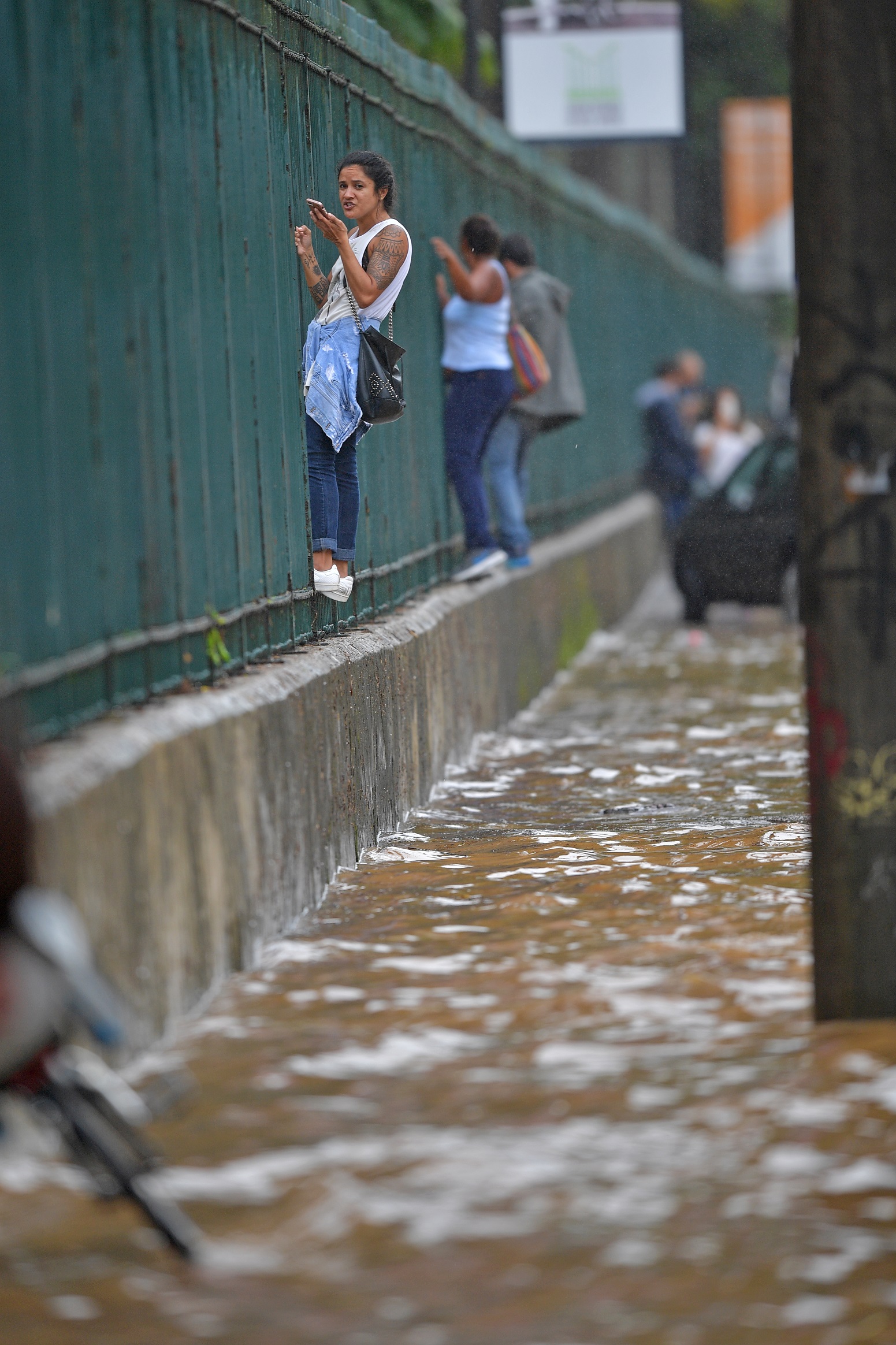 Mulheres se penduram nas grandes do Jardim Botânico para fugir das ruas alagadas. Foto Carl de Souza/AFP