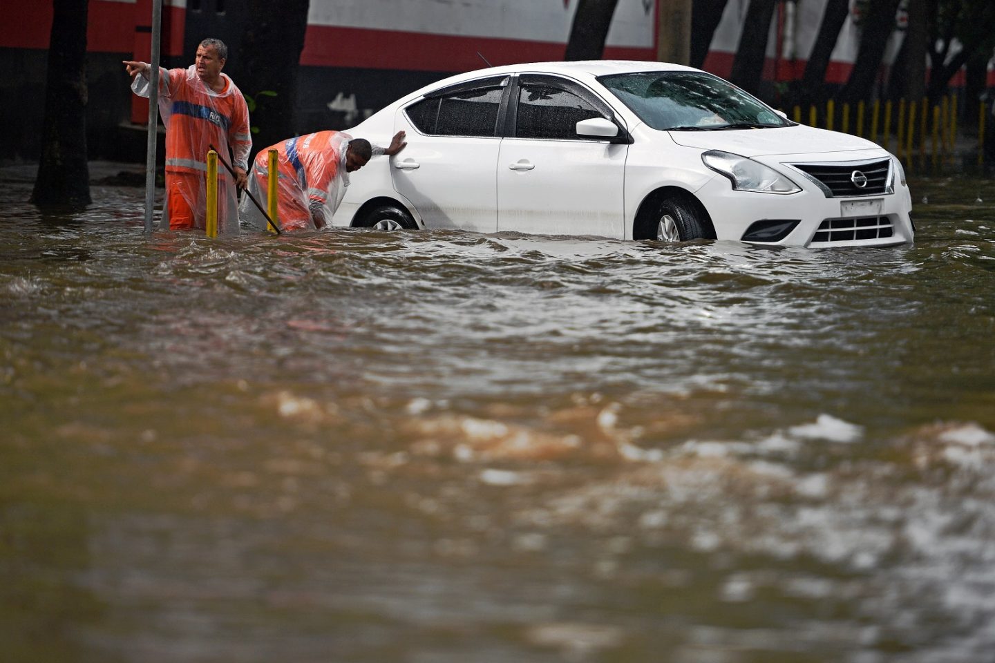 Funcionários da Comlurb tentam desobstruir os bueiros com as ruas da cidade alagadas. Foto Carl de Souza/AFP