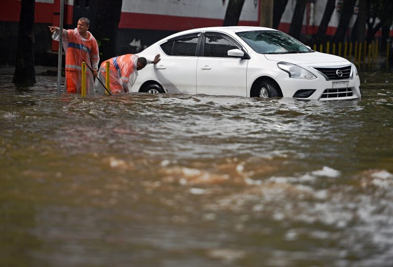 Funcionários da Comlurb tentam desobstruir os bueiros com as ruas da cidade alagadas. Foto Carl de Souza/AFP