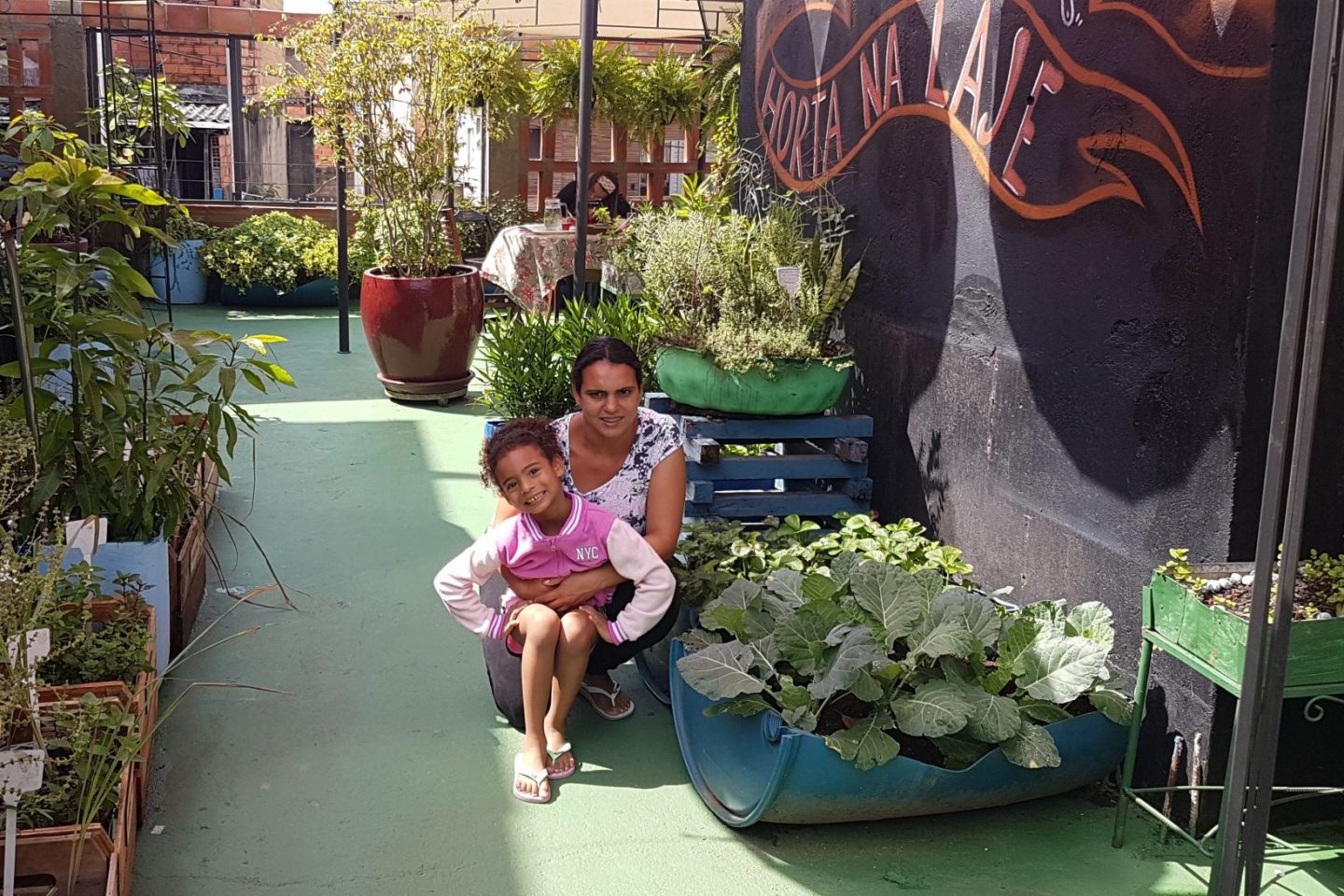 Natália com a filha Júlia: horta com manjericão, alface, rúcula e coentro na sua laje em Paraisópolis após passar pelo projeto (Foto: Florência Costa)