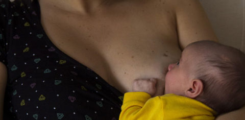 Foto alternativa de mulher amamentando o filho. Ela aparece com a criança no colo e olha para ela.