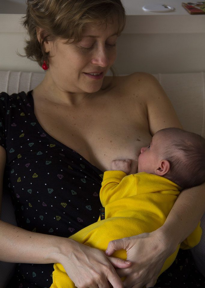 Foto alternativa de mulher amamentando o filho. Ela aparece com a criança no colo e olha para ela.