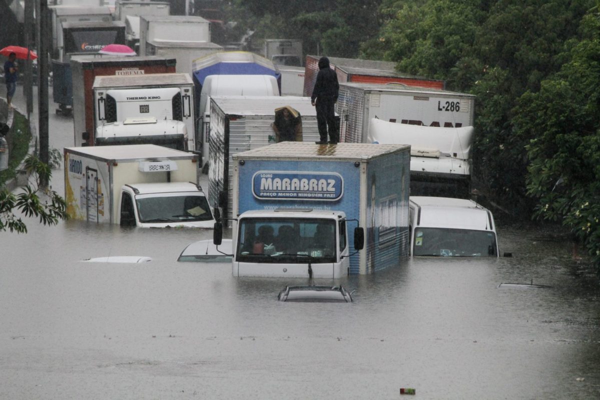 Carros encobertos pela água e caminhões com água na altura da cabine em rua alagada pela chuva forte em São Paulo