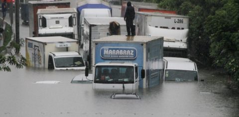 Carros encobertos pela água e caminhões com água na altura da cabine em rua alagada pela chuva forte em São Paulo