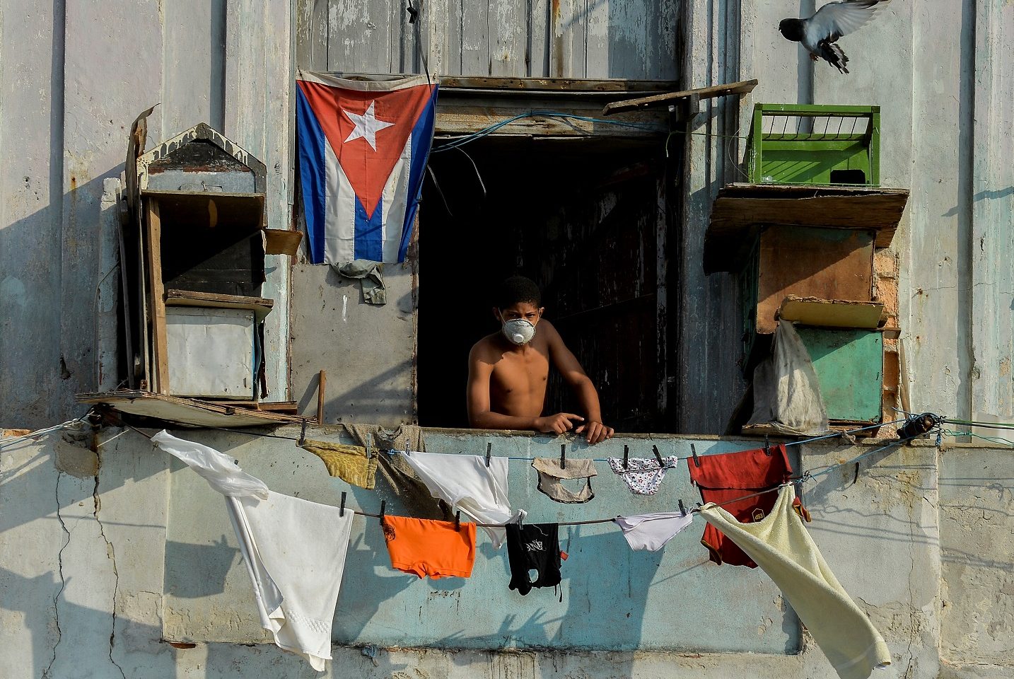 Homem usa máscara facial na varanda em Havana. As autoridades cubanas dizem que o embargo econômico dos EUA vem dificultando o combate à covid-19. Foto Yamil Lage/AFP