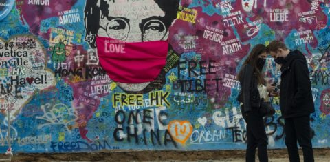 Um casal conversa em frente ao "Muro de Lennon", em Praga, que, em tempos de Covid-19, também usa a sua máscara. Foto Michal Cizek/AFP