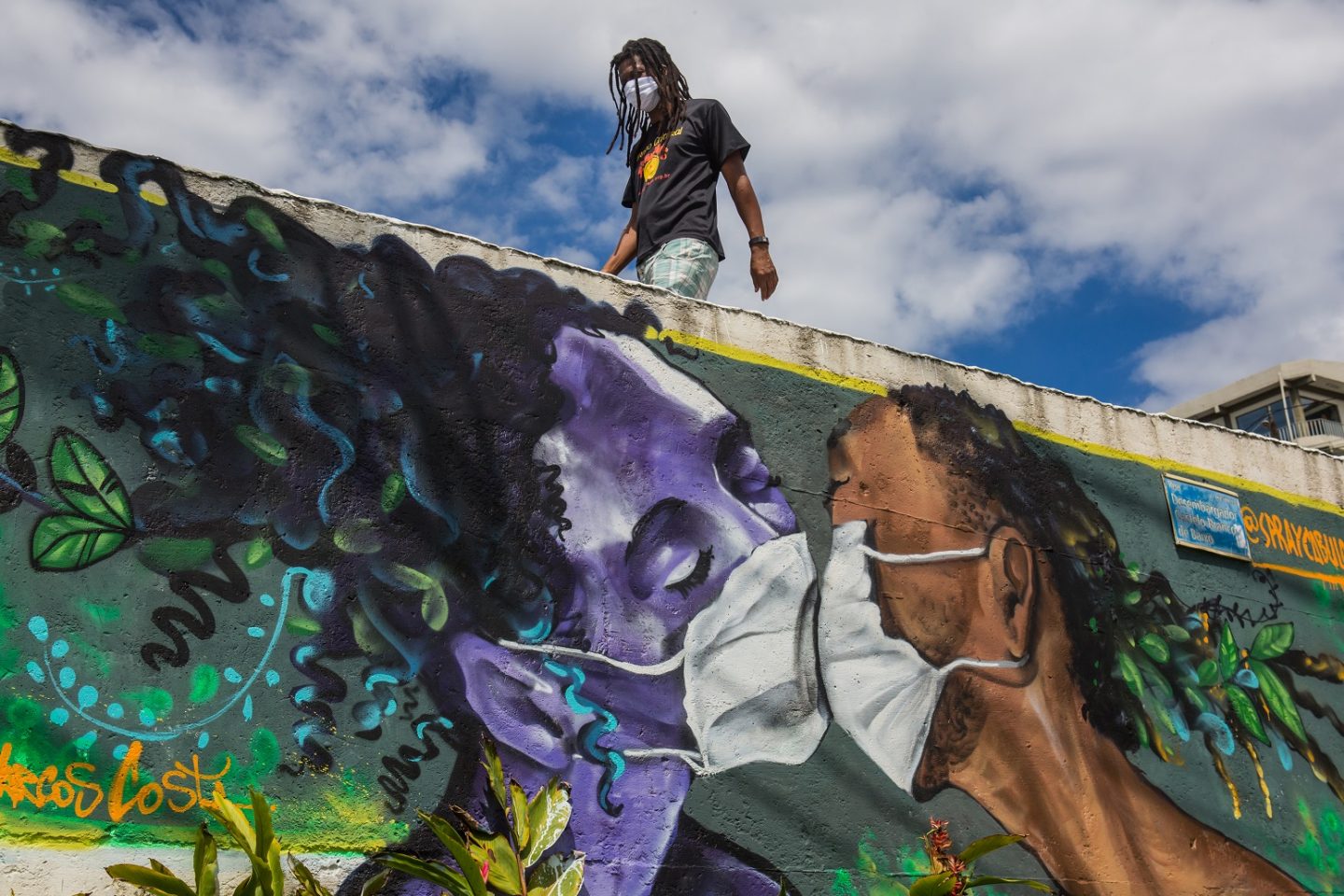 Um homem usando máscara passa por um grafite do artista Marcos Costa, ou Spraycabuloso, na entrada da favela Solar de Unhão, em Salvador. Foto Antonello Veneri/AFP