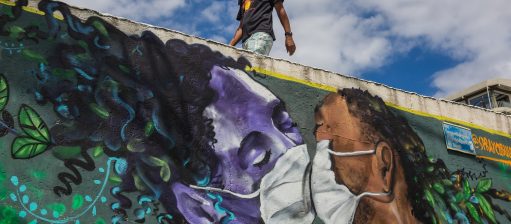 Um homem usando máscara passa por um grafite do artista Marcos Costa, ou Spraycabuloso, na entrada da favela Solar de Unhão, em Salvador. Foto Antonello Veneri/AFP