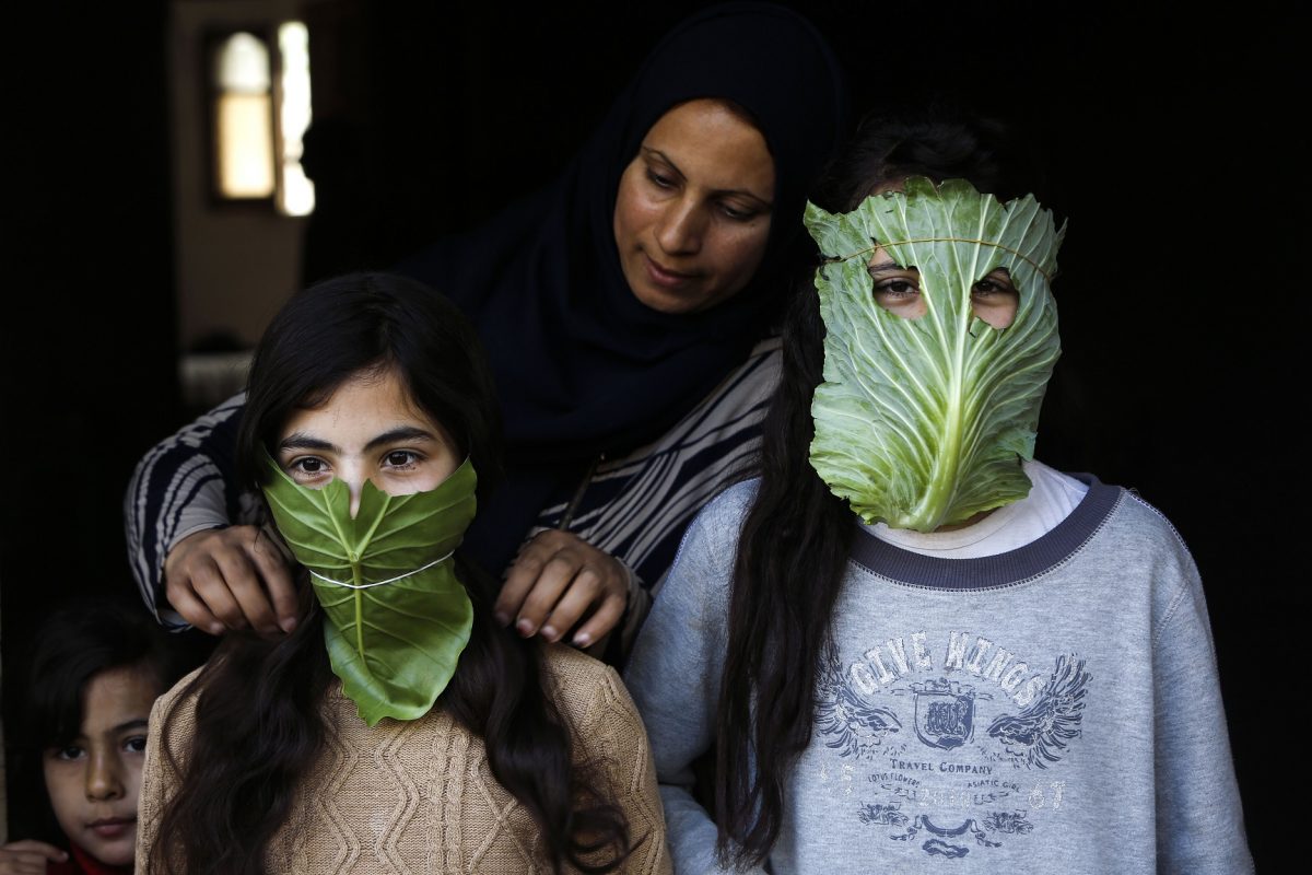 Uma mãe palestina entretém seus filhos com máscaras improvisadas de repolho enquanto cozinha em Beit Lahia, no norte da Faixa de Gaza. Foto Mohammed Abed/AFP