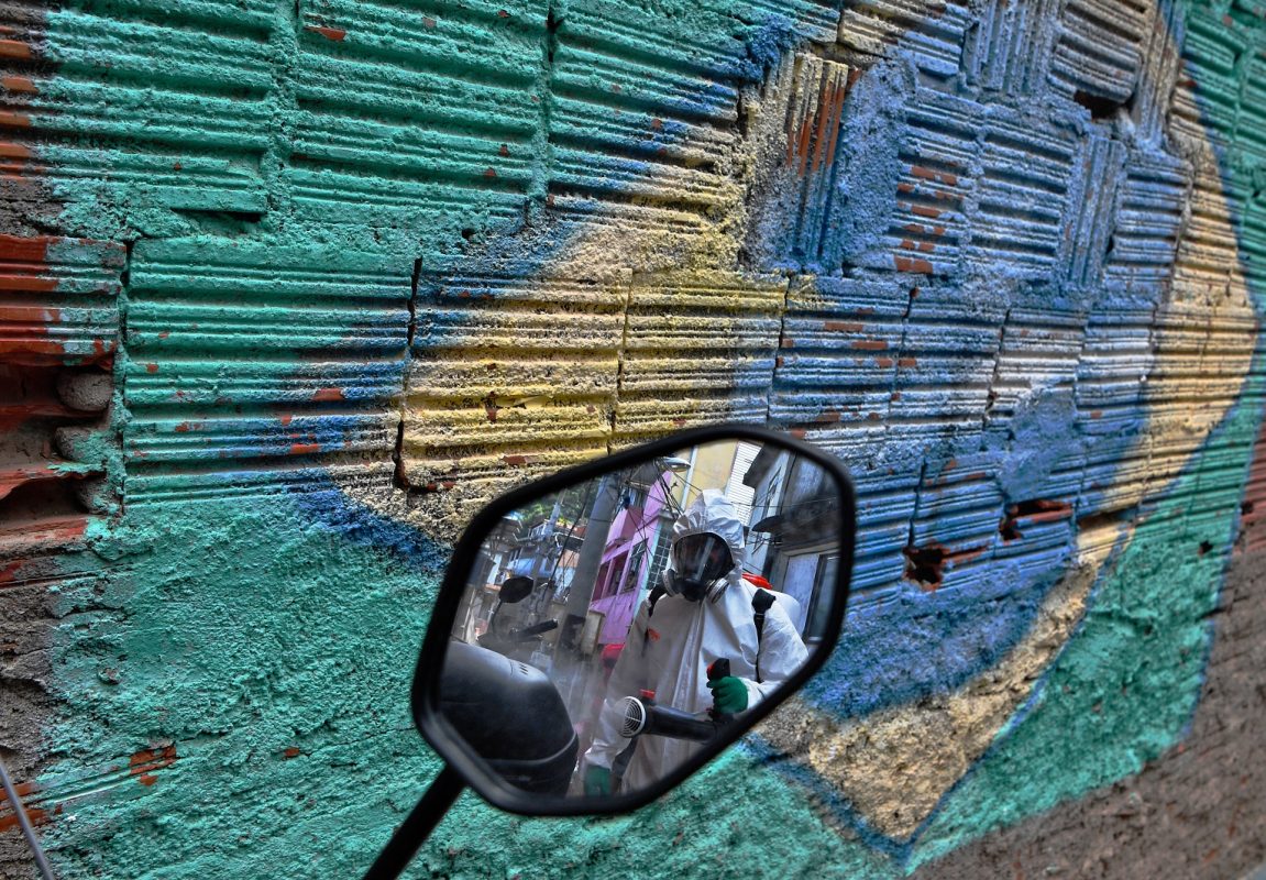 Um homem é refletido no espelho de uma motocicleta enquanto desinfeta uma área dentro da favela de Babilônia,na Zona Sul do Rio de Janeiro. Foto Carl de Souza/AFP