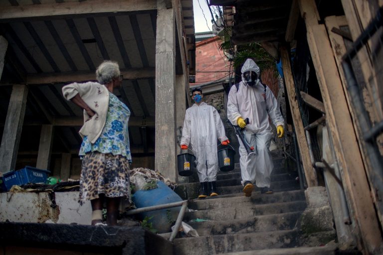 Uma mulher observa voluntários que desinfetam um beco na favela de Santa Marta, no Rio de Janeiro. Foto Mauro Pimental/AFP