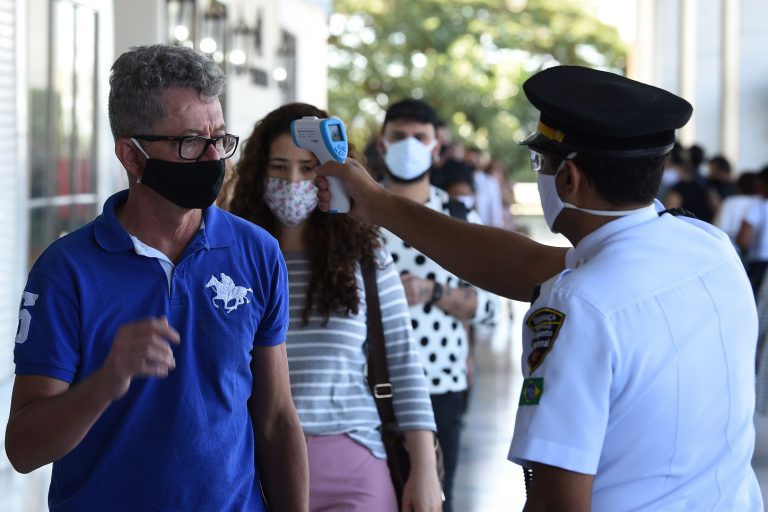 Funcionário de um shopping em Brasília checa a temperatura dos clientes no primeiro dia de funcionamento do comércio na cidade. Foto Evaristo Sá/AFP