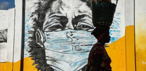 Na Tanzânia, uma mulher carrega uma cesta na cabeça enquanto caminha em frente a um grafite pintado pelo grupo de artistas Wachata para aumentar a conscientização sobre o uso de máscaras na pandemia. Foto Ericky BONIPHACE / AFP
