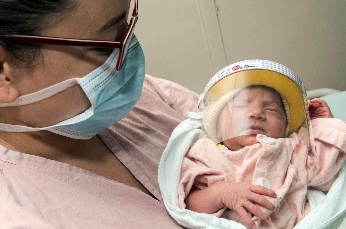 Uma mulher usando máscara facial posa com seu bebê recém-nascido - usando um escudo facial - na unidade de Neonatologia do Hospital México em San Jose, na Costa Rica. Foto Ezequiel Becerra/AFP