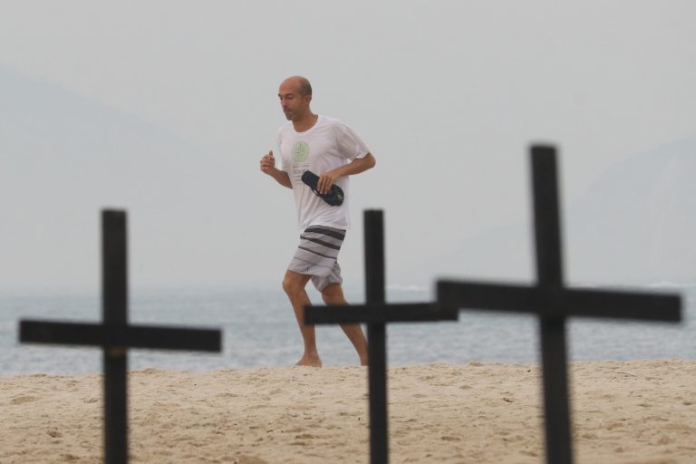 Banhista corre na praia de Copacabana em meio às cruzes plantadas pela ONG Rio de Paz em protesto contra a política de combate ao covid-19 na cidade e no país. Foto Dikran Junior/AGIF