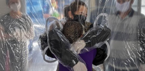 Elisabete Nagata (em cima) abraça sua cunhada Luiza Nagata, de 76 anos, através de uma cortina de plástico transparente em um lar de idosos em São Paulo. Foto Nelson Almeida/AFP