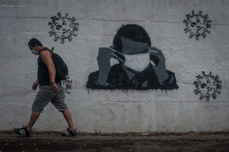 Homem de máscara passa em frente ao grafite feito pelos coletivos dos artistas Nogenta e contraconsiencia, no Rio Comprido. As imagens representam o presidente Bolsonaro. Foto Allan Carvalho/NurPhoto