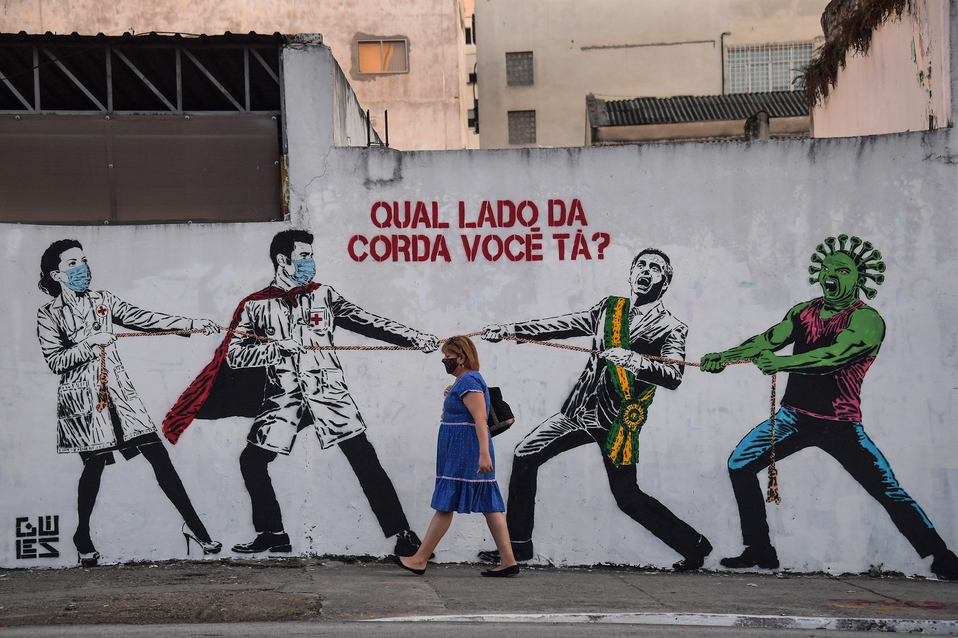 Em São Paulo, mulher passa em frente a um grafiti representando a batalha contra o coronavírus: "De que lado você está?". Foto Nelson Almeida/AFP