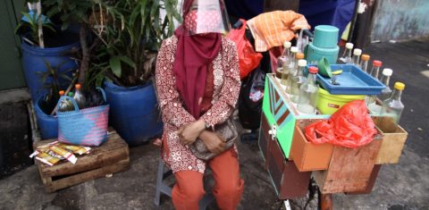 Uma vendedora de Jamu, bebida tradicional à base de plantas da Indonésia, usa máscara e protetor facial em Jacarta. Foto Aditya Irawan/NurPhoto
