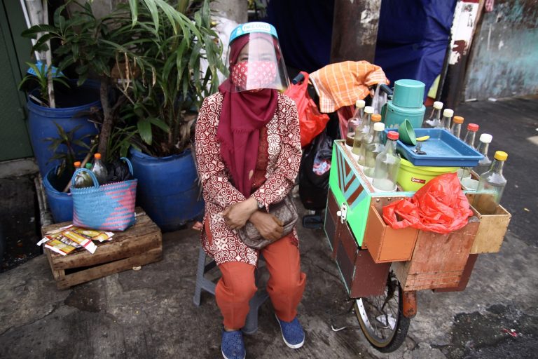Uma vendedora de Jamu, bebida tradicional à base de plantas da Indonésia, usa máscara e protetor facial em Jacarta. Foto Aditya Irawan/NurPhoto