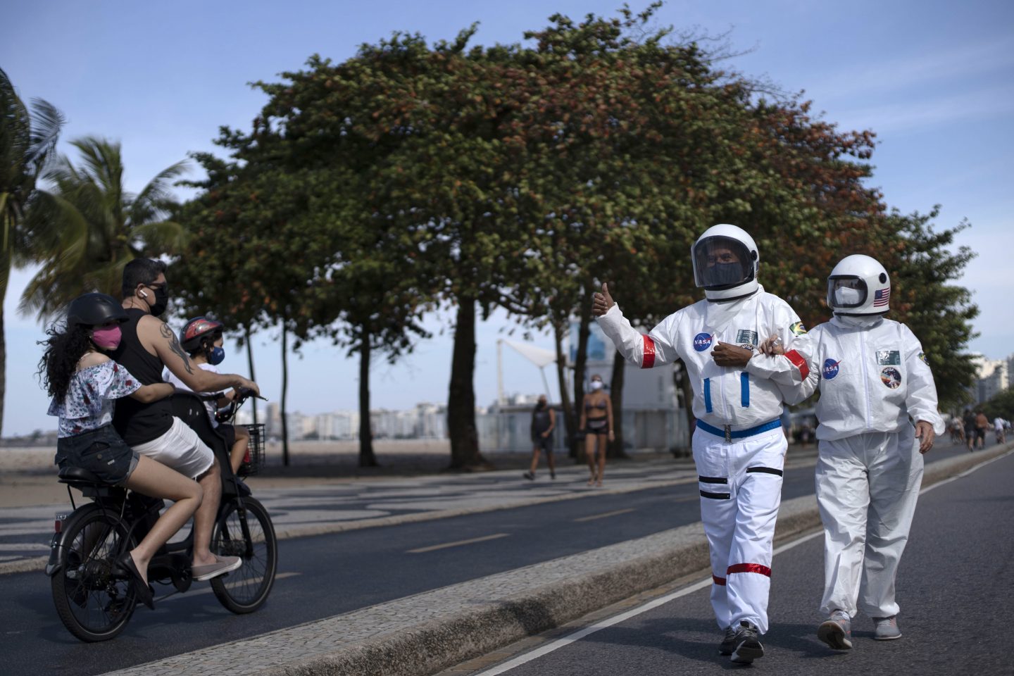 Casal passeia com roupa de astronauta pela orla do Leme: Rio tem queda nos casos, mas isolamento ainda é necessário. Foto de Mauro Pimentel (AFP)