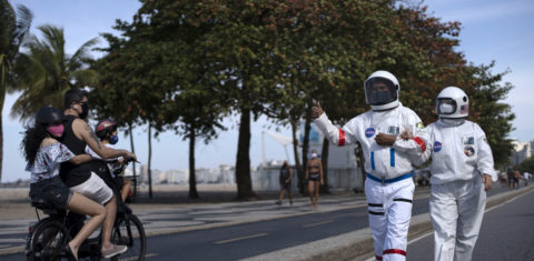 Casal passeia com roupa de astronauta pela orla do Leme: Rio tem queda nos casos, mas isolamento ainda é necessário. Foto de Mauro Pimentel (AFP)