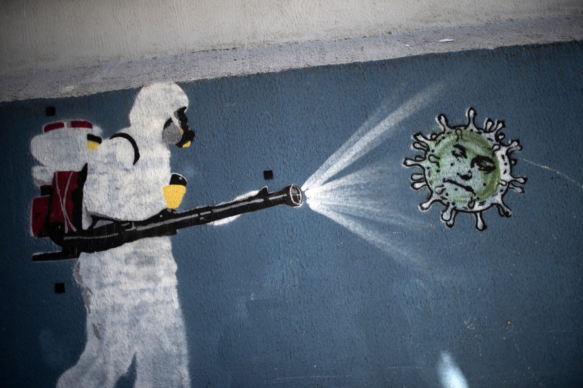 Mural na Tijuca, no Rio de Janeiro, representa um homem em traje de proteção pulverizando desinfetante em um coronavírus com o rosto do presidente Bolsonaro. Foto Mauro Pimentel/AFP