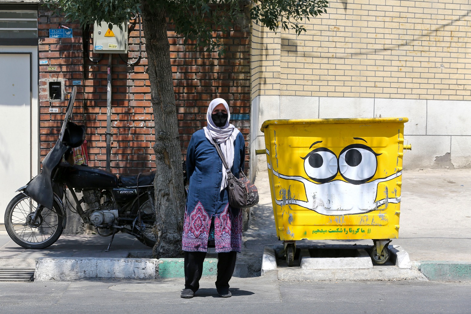 Em um bairro no sul de Teerã, capital do Irã, uma mulher passa ao lado de uma caixa de coleta de lixo pintada com uma máscara de proteção contra a covid-19. Foto Atta Kenare/AFP