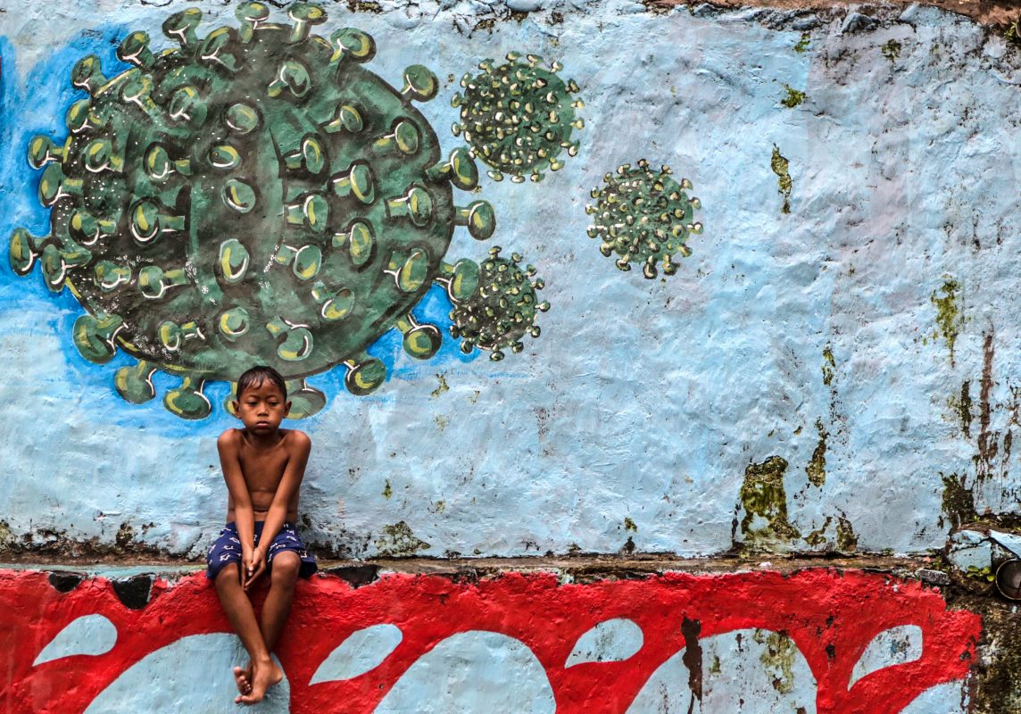 Na Indonésia, um menino descansa sentando em frente a um mural que representa o coronavírus. Foto Aditya Aji/AFP
