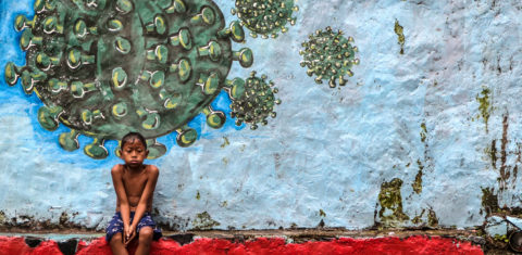 Na Indonésia, um menino descansa sentando em frente a um mural que representa o coronavírus. Foto Aditya Aji/AFP