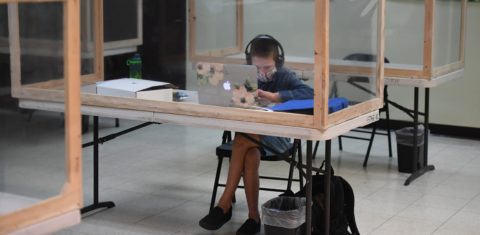 Na Califórnia, um aluno acompanha remotamente a aula ao online do professor da escola regular em uma mesa separada dos outros por barreiras de plástico na STAR Eco Station Tutoring. Foto Robyn Beck/AFP