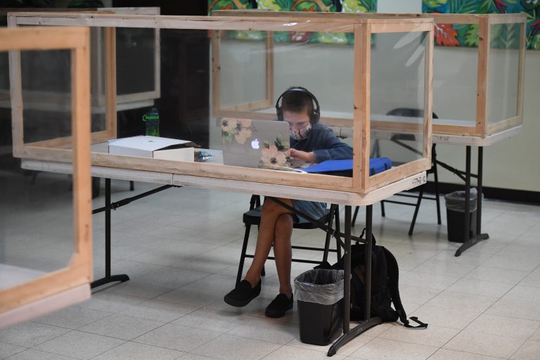 Na Califórnia, um aluno acompanha remotamente a aula ao online do professor da escola regular em uma mesa separada dos outros por barreiras de plástico na STAR Eco Station Tutoring. Foto Robyn Beck/AFP