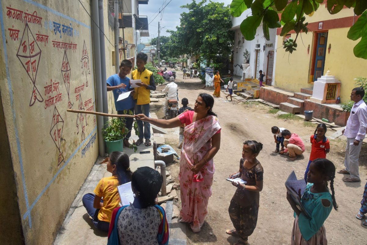 Professora usa parede para dar aula a alunos em vila na Índia: crianças fora da escola e sem acesso à merenda (Foto: AFP)