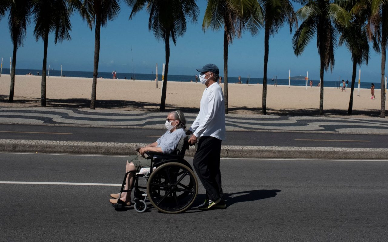 Idosa conduzida por acompanhante na praia de Copacabana: estudo da Fiocruz indica aumento no número de idosos que faleceu fora de hospitais, em sua residência ou em abrigos - 78% no município e 54% no estado (Foto: Fábio Teixeira/Nur Photo/AFP)