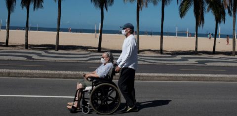 Idosa conduzida por acompanhante na praia de Copacabana: estudo da Fiocruz indica aumento no número de idosos que faleceu fora de hospitais, em sua residência ou em abrigos - 78% no município e 54% no estado (Foto: Fábio Teixeira/Nur Photo/AFP)