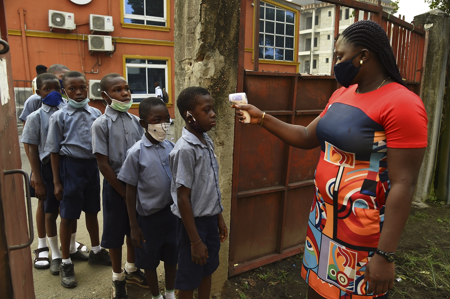 Professora primária mede a temperatura dos alunos no portão do berçário Obele-Odan, em Surulere, Lagos, na Nigéria. Foto Pius Utomi Ekpei/AFP. Janeiro/2021