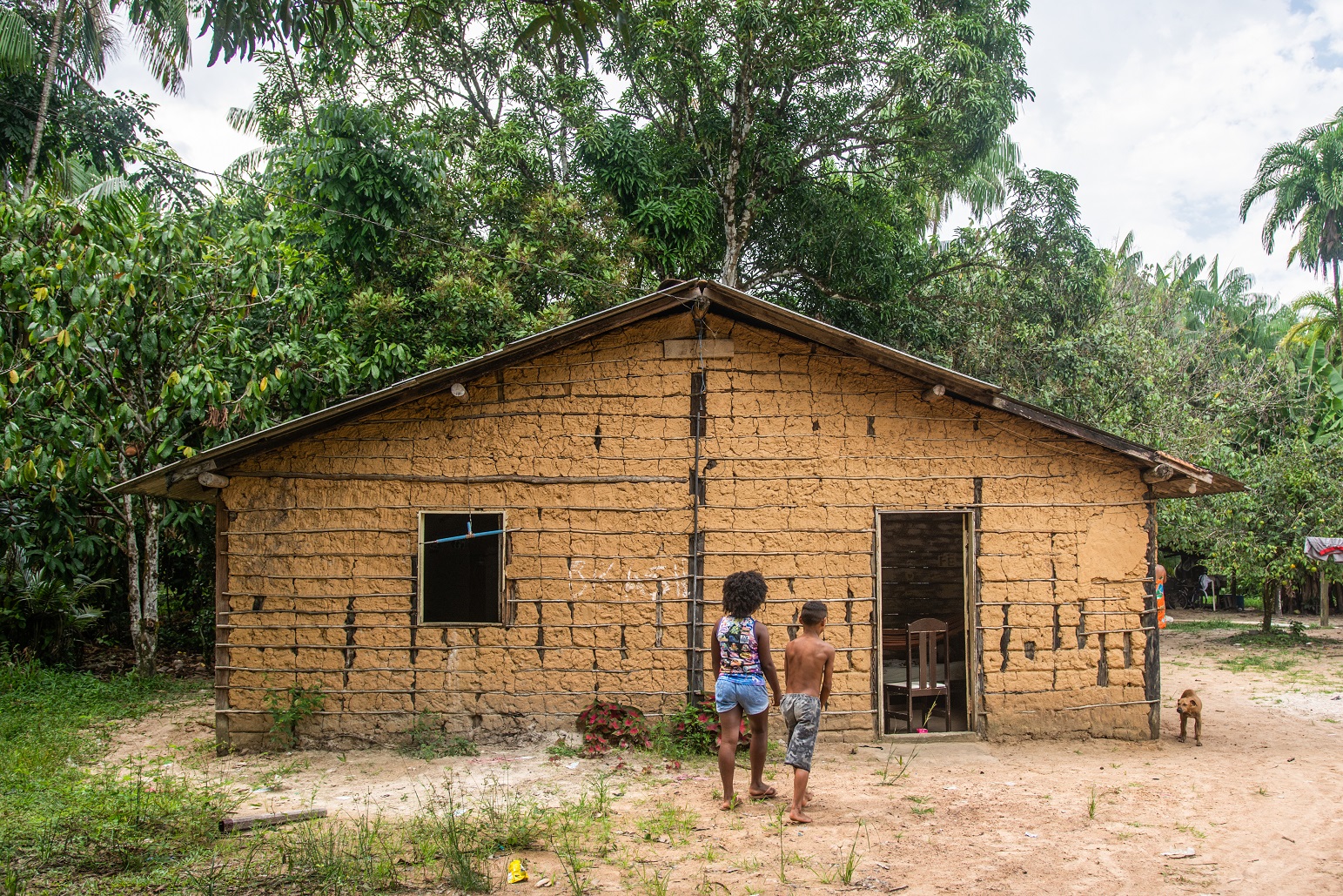 Two people and a dog in front of a house in the Abacatal Quilombola Community, in Ananindeua, Pará.