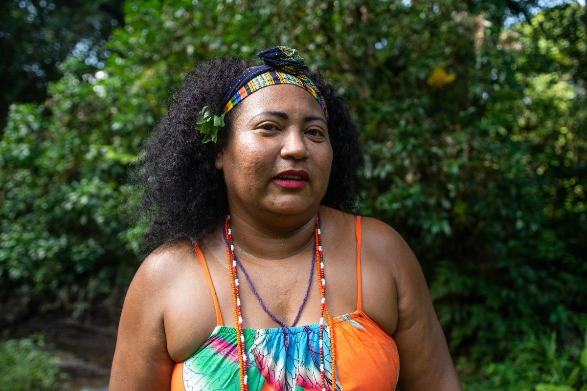 Vanuza Cardoso wears a headband, an orange top, and beaded necklaces.