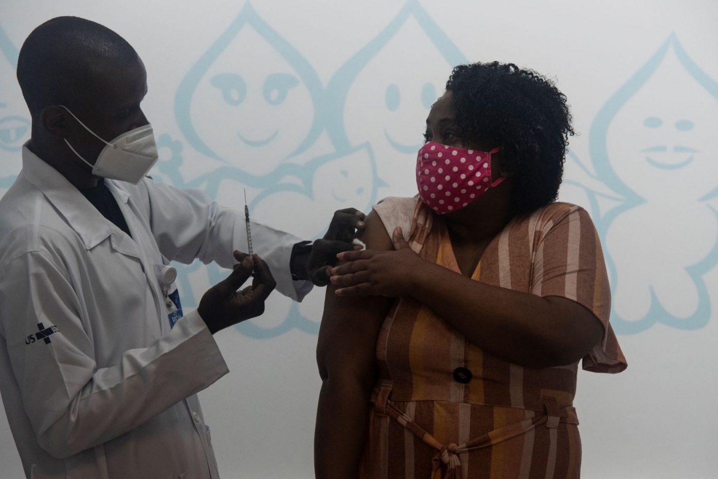 Profissional de saúde, com máscara cirúrgica, vacina moradora do Rio com máscara de pano com camadas: pesquisa com infectados confirmou eficácia da máscara para evitar transmissão (Foto: Fábio Teixeira/NurPhoto/AFP -13/05/2021)