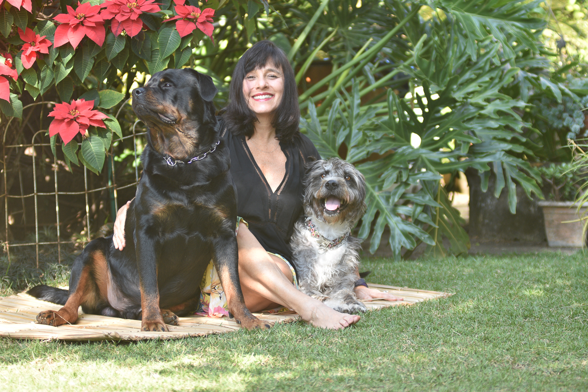Carla Mott sentada em uma esteira no gramado com dois cachorros